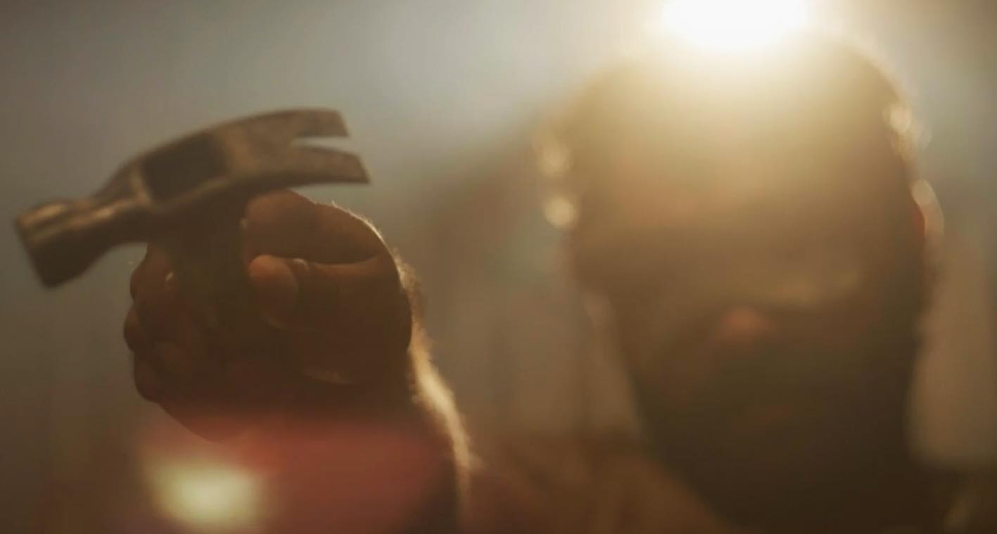 Screenshot from Marlu Man. Shows Marlu Man in a kangaroo skin mask holding a hammer pointed towards the camera.